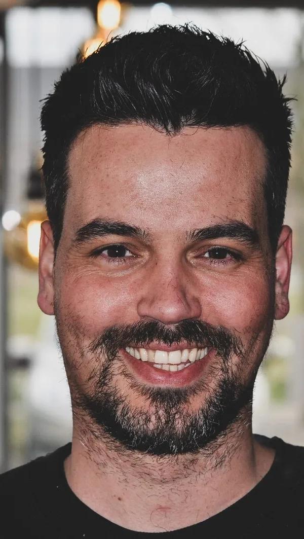 Frontaal portret van klant met korte zijkanten en volle baard, lachend in barbershop