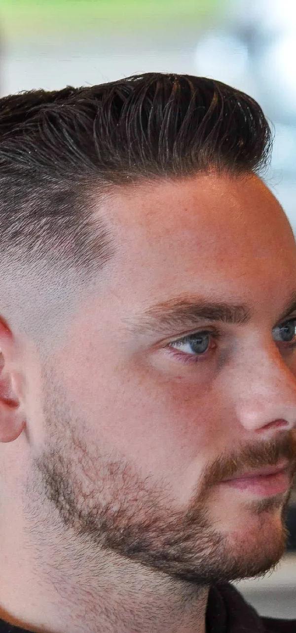 Klassieke side part met skin fade en lichte stoppels, profielportret